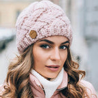 Light pink knitted beanie hat with chunky cable texture and brown brand patch