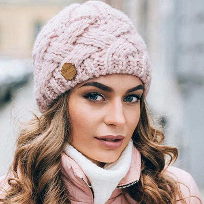 Light pink knitted beanie hat with chunky cable texture and brown brand patch