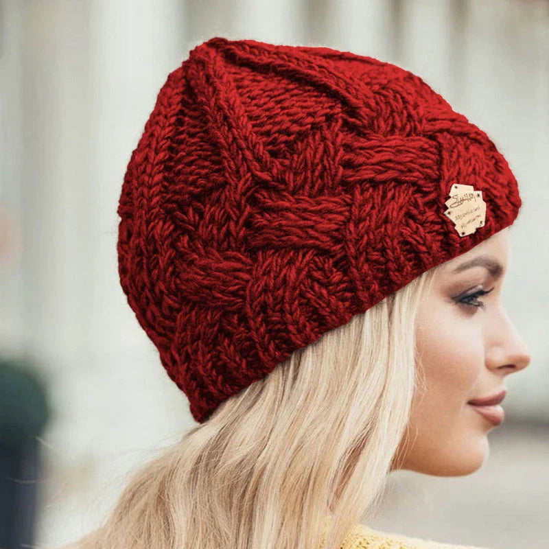 Red cable-knit beanie hat with small brown brand patch