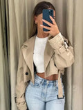 Women’s short light-brown trench coat worn over a white top, belted waist