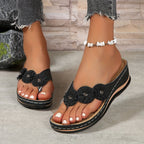 Women's wedge sandals in black with floral front detail, cushioned footbed, thong toe